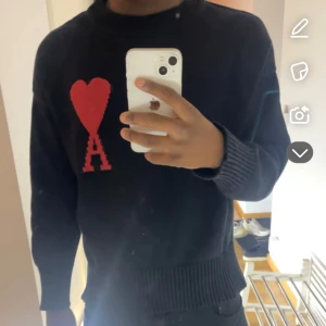 Svart stickad tröja från Ami Paris med rött hjärta - Säljer en svart stickad tröja från Ami Paris med ett stort rött hjärta och bokstaven A på bröstet. Tröjan har rund halsringning och ribbade muddar vid ärmslut och nederkant. Perfekt för dig som gillar stilrena plagg med en twist.