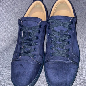 Mörkblå sneakers från Christian Louboutin - Snygga mörkblå sneakers i mocka från Christian Louboutin med ton-i-ton snörning och broderad logga på hälen. Skorna har rund tå och platt sula, samt ljus insida för en stilren kontrast.