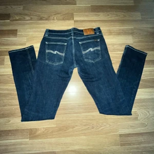 Nudie Jeans 30/34 - Dessa blåa nudie jeans i storlek 30/34 erbjuder en perfekt kombination av stil och komfort. Med en modern passform och tidlös design är de ett utmärkt val för både vardag och fest. Jeansens klassiska blå färg och högkvalitativa material gör dem hållbara och lätta att matcha med olika plagg. Kontakta mig gärna för att diskutera priser och andra detaljer!