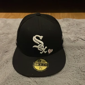 Svart keps från New Era 59FIFTY Chicago White Sox - Svart 59FIFTY keps från New Era med Chicago White Sox-logga broderad framtill, vita och röda broderade detaljer samt texten 'Love & Hustle Game' på sidan. Platt skärm och broderade märkesloggor på sidorna.
