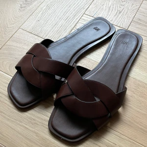 Bruna sandaler med flätad rem från H&M - Säljer ett par stilrena bruna sandaler från H&M med breda, korslagda remmar och fyrkantig tå. Stl 40 men passar bra på mig som har stl 39🤎