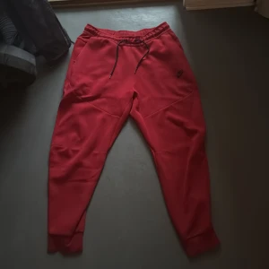 Röda mjukisbyxor från Nike - Säljer ett par röda mjukisbyxor från Nike i storlek L. Byxorna har snörning i midjan och en dragkedjeficka bak. Perfekta för chill eller träning. Klassisk Nike-logga på framsidan.