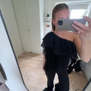 Svart oneshoulder topp med volang - Säljer nu denna svarta oneshoulder toppen från Noella!! Går inte att få tag på längre. Passar perfekt både till sommar och vinter. Storlek M men passar även som S. Använd ca 2 gånger. Hör av dig vid frågor och funderingar!🖤