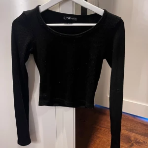 Svart croppad långärmad topp från FB Sister - Säljer en svart croppad långärmad topp från FB Sister. Toppen är ribbad och har en rund halsringning. Perfekt att styla med höga jeans eller kjol.