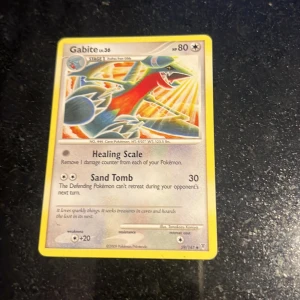 Gabite - Samlarkort med Gabite, en drakliknande Pokémon från den populära Pokémon-serien. Perfekt för dig som gillar att samla, byta eller spela Pokémonkort. Kortet har 80 HP och två attacker: Healing Scale och Sand Tomb. Ett måste för Pokémon-fans!
