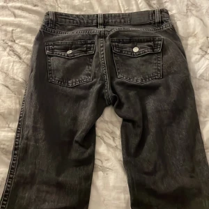 Svarta lågmidjade  bootcut jeans från Gina - Säljer ett par svarta bootcut jeans med klassiska fem fickor och silverfärgade knappar. Jeansen har en något utsvängd passform nertill och låg midja. Perfekta för dig som gillar en tidlös och avslappnad stil.