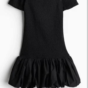 Svart kortklänning med volang - Säljer en svart kortklänning som är offshoulder och med volang nertill. Klänningen har korta ärmar och en luftig, ballongliknande kjol. Perfekt för dig som gillar en stilren och trendig look. Helt oanvänd, prislappen är kvar och pris kan diskuteras💕