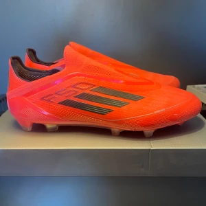 Adidas F50 fotbollsskor i neonröd - Säljer ett par Adidas F50 fotbollsskor i en riktigt snygg neonröd färg med svarta detaljer. Skorna har låg profil, platt sula med dobbar och är tillverkade i syntetmaterial. Perfekta för dig som vill sticka ut på planen!