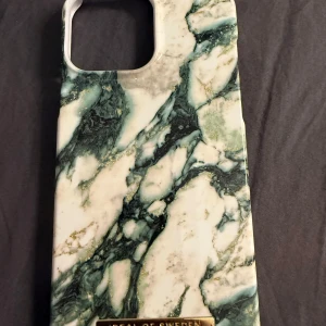 Grönvit marmorerat mobilskal från iDeal of Sweden - Snyggt mobilskal med marmormönster i grönt, vitt och inslag av guld från iDeal of Sweden. Skalets yta har en lyxig känsla och en guldfärgad logga framtill. Perfekt för dig som vill ge mobilen en trendig look. Passar till 13 pro max och 14 plus 