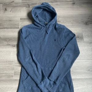 Blå hoodie från Polo Ralph Lauren - Säljer en blå hoodie från Polo Ralph Lauren med ribbad struktur och klassisk huva med dragsko. Väldigt sparsamt använd och därmed inga defekter, väldigt mysigt matrial, perfekt för kalla sommarkvällar☀️