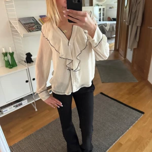 Vit blus med volang och svarta detaljer - Säljer en vit blus med volangkant och svarta sömmar längs volangen. Från Zara och är sparsamt använd!❤️