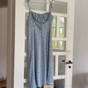 Blommig blå långklänning från Adoore - Säljer en ljusblå långklänning från Adoore med smala axelband och blommigt mönster. Helt oanvänd, alla lappar kvar.