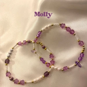 Molly bracelet - 2 pack - Två elastiska armband med lila och vita pärlor samt små guldfärgade detaljer. 