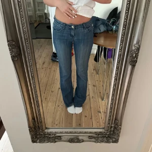 Blå bootcut jeans - Säljer ett par klassiska blå bootcut jeans  med låg midja. Jeansen har fem fickor, dragkedja och knapp framtill samt snygga detaljer på bakfickorna. Perfekta till vardags för en avslappnad look. Är klippta till att passa mig som är 165cm