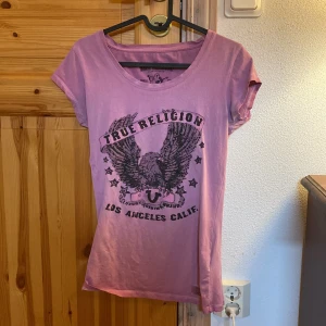 t-shirt från True Religion - Säljer en t-shirt från True Religion med svart tryck och glittriga detaljer framtill. T-shirten har rund halsringning och korta ärmar. Perfekt för dig som gillar streetwear och vill sticka ut lite extra.