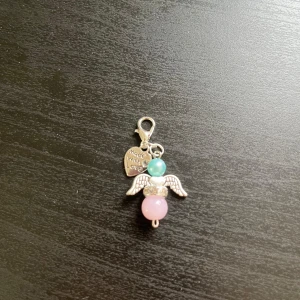 Ängelberlock med pärlor och vingar🩵 - Söt berlock formad som en ängel med silverfärgade vingar, en rosa och en turkos pärla samt ett litet hjärta med texten 'Made with love'. Perfekt som accessoar till väska eller smycke🩵.