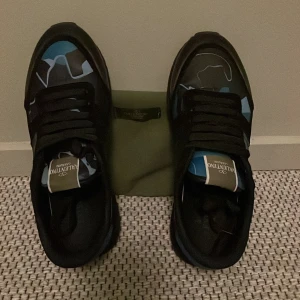 Valentino Rockrunner sneakers med blått kamouflagemönster - Säljer ett par Valentino Rockrunner sneakers med svart och blått kamouflagemönster du får med extra snören från valentino Perfekta för dig som vill sticka ut med exklusiva sneakers. Kan pruta ner priset skriv om ni har några frågor