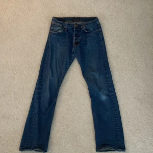 Nudie Jeans - Säljer ett par klassiska blå jeans från Nudie Jeans, klassisk blå tvätt och kopparorange sömmar. Liten slitning i skrevet men syns inte när man har på sig de. Hör gärna av er om frågor.