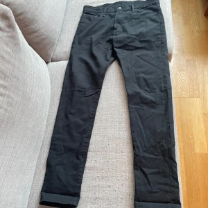 Svarta jeansbyxor från Levi's 501 - Säljer ett par klassiska svarta Levi's 501 jeans med raka ben och fem fickor. Byxorna har normal passform, knappgylf och är tillverkade i ett slitstarkt jeanstyg. Perfekta för dig som gillar tidlös stil och vill ha ett par jeans som funkar till allt.