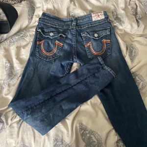  jeans från True Religion - Säljer ett par klassiska blå jeans från True Religion med ikoniska bakfickor och kontrastsömmar i orange. De är skinny jeans och passar som en M. Säljer då de inte passar mig längre. 