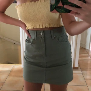 Grön kort jeanskjol - Gina tricot  - Säljer en mörkgrå  kort jeanskjol med två stora bakfickor och bälteshällor. Kjol är använd fåtal gånger och är i bra skick. Är i storlek 34