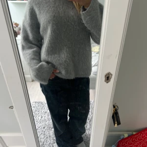 Grå fluffig stickad tröja - Mysig grå stickad tröja med lång ärm och rund hals. Tröjan har en fluffig och mjuk känsla, perfekt för sommarkvällar osv. Passformen är normal och modellen är enkel utan synliga detaljer eller mönster.