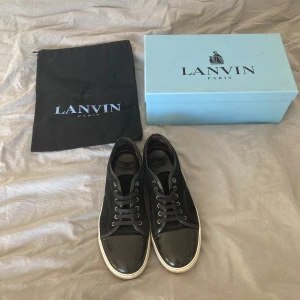 Svarta sneakers från Lanvin med lackad tå - Säljer ett par svarta sneakers från Lanvin med snygg lackad tå och vita sulor. Skorna har snörning och klassisk design, levereras med originalpåse och låda. Perfekta för dig som gillar stilrena och exklusiva sneakers.