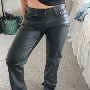 Svarta skinnbyxor med normal passform - Säljer ett par svarta skinnbyxor med klassisk femficksdesign och raka ben. Byxorna har normal passform och stängs med dragkedja och knapp i midjan. Perfekta för dig som vill ha en stilren och edgy look.