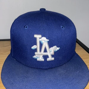 Blå LA Dodgers keps från New Era - Säljer en blå LA Dodgers keps från New Era med broderad LA-logga och molndetaljer framtill. På sidan finns World Series 2020-märke och MLB-logga bak. Klassisk passform och platt skärm.