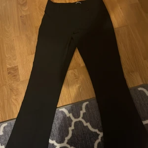 Svarta kostymbyxor med utsvängda ben - Snygga svarta kostymbyxor med normal passform och raka ben. Byxorna har diskreta fickor framtill och stängs med knapp och dragkedja. Perfekta för en stilren look därmed HAR EJ ANDVÄNT DOM
