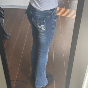 Bootcut jeans - Säljer ett par blå bootcut jeans med snygg broderad bakficka och knappdetalj. 