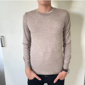 Beige rundhalsad tröja från Oscar Jacobson - Säljer en stilren beige rundhalsad tröja från Oscar Jacobson i storlek M. Tröjan är tunnstickad med långa ärmar och ribbade muddar vid ärmslut och nederkant. Perfekt för lager-på-lager och passar till många olika outfits.