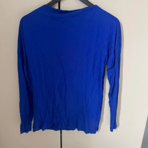 Kornblå långärmad tröja Filippa k  - En enkel och stilren kornblå långärmad tröja. Perfekt att matcha med jeans eller kjol för en avslappnad look. Tröjan har en rak passform och är tillverkad i ett mjukt material.
