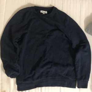 Mörkblå sweatshirt från Kappahl - En enkel och stilren mörkblå sweatshirt från Kappahl. Tröjan har rund halsringning, långa ärmar och ribbade muddar vid ärmslut och nederkant. Perfekt för en avslappnad och bekväm stil.