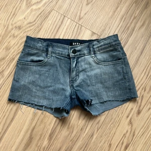 Lågmidjade jeansshorts  - Säljer ett par klassiska blå jeansshorts från DKNY med råa, fransiga benslut och femficksmodell. Shortsen har låg midja och knappgylf. Perfekta för varma dagar och enkel att matcha med olika toppar.