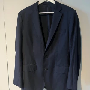 Mörkblå kavaj i merinoull  Loro Piana - Snygg mörkblå kavaj i 100% New Zealand merinoull, tillverkad i Italien. Klassisk modell med två knappar framtill, fickor med lock och bröstficka. Perfekt för bal eller fest.