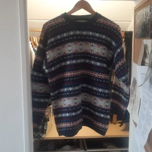 Mönstrad stickad tröja från Jackport - Säljer en stickad tröja från Jackport med klassiskt mönster i blått, vitt och rött. Tröjan har rund halsringning och långa ärmar. Perfekt för kyliga dagar och vintage.