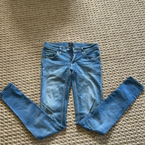 Blå skinny jeans från Tiger of Sweden - Säljer ett par klassiska blå skinny jeans från Tiger of Sweden, modell Slender. Jeansen har fem fickor, dragkedja och knapp framtill samt diskret logga bak i midjan. Perfekta för dig som gillar en tight passform och stilren look.