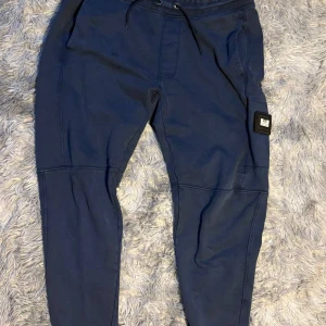 Blå mjukisbyxor från Weekend Offender - Säljer ett par blå mjukisbyxor från Weekend Offender i storlek L. Byxorna har dragsko i midjan, sidofickor och en patch med logga på benet. Perfekta för chill dagar eller när du vill vara bekväm.