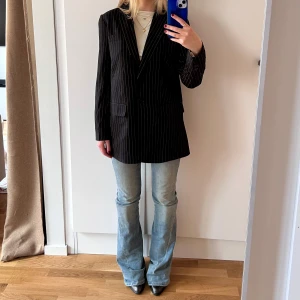 Svart randig kavaj/blazer från Pieces - Säljer en svart kavaj med vita tunna ränder från Pieces. Kavajen har klassisk passform, långa ärmar och två knappar framtill. Perfekt för en stilren look och funkar lika bra till jeans som till kostymbyxor. Storlek XS. Jag är 158cm för referens, bär ca 7cm-klackar på den här bilden.