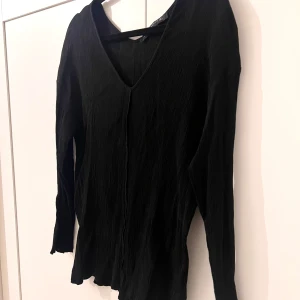 Svart v-ringad blus - Säljer en svart blus med v-ringning och lång ärm. Tyget är lätt och har en skrynklig struktur som ger en avslappnad känsla. Perfekt att styla med jeans eller kjol för en enkel men snygg look.