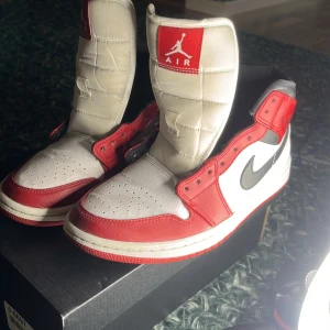 Nike Air Jordan 1 Mid röd/vit/svart - Säljer ett par Nike Air Jordan 1 Mid i rött, vitt och svart. Klassisk high-top modell med svart swoosh, röd yttersula och perforerad tå. Skorna har snörning och ikonisk Air Jordan-logga på plösen. Perfekta för dig som gillar streetwear och sneakerskultur. Snören tillkommer såklart! Hör av er vid fler frågor