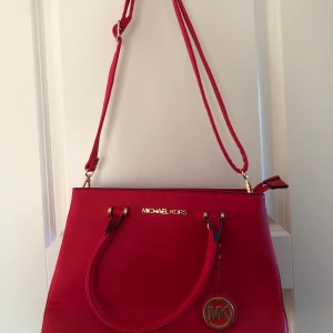 Röd axelväska från Michael Kors - Snygg röd axelväska från Michael Kors med guldfärgade detaljer och logotyp. Väskan har både handtag och justerbar axelrem samt flera fack inuti för bra organisering. Perfekt för dig som vill ha en stilren och trendig accessoar ❤️