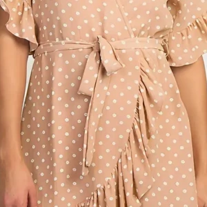 Beige prickig omlottklänning med volang - Supersöt beige omlottklänning med vita prickar och volangdetaljer. Klänningen har knyt i midjan och korta ärmar med volang. Perfekt för en somrig look!