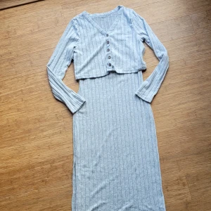 Supergosig Ljusgrå ribbad 2-delat set nytt - Säljer en ljusgrå ribbad klänning med smala axelband och tillhörande croppad kofta med v-ringning och knappar framtill. Setet är supermjukt och stretchigt, perfekt för en avslappnad men stilren look. OANVÄNT, för litet för mig tyvärr som är 40-42. Uppskattar detta i storlek 38!