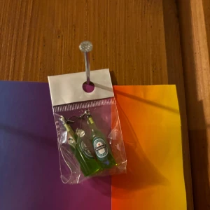 Örhängen med gröna flaskor - Unika örhängen formade som gröna flaskor med etikett, perfekta för dig som vill sticka ut. Rolig och annorlunda accessoar som garanterat drar blickarna till sig.