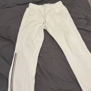 Vita mjukisbyxor från Hugo boss med randdetalj - Säljer ett par vita mjukisbyxor från BOSS med elastisk midja och dragsko. Byxorna har raka ben, fickor med dragkedja och en broderad BOSS-logga. Snygg rand i svart och beige längs ena benet ger extra stil. Köpte dom på Hennings för ungefär 6 månader sedan för 2200 mitt pris är 950 skick är 9/10 och fraktas direkt vid köp