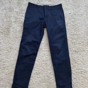 Mörkblå chinos - Snygga mörkblå chinos med klassisk passform och raka ben. Byxorna har två fickor fram och två bakfickor med knapp. Perfekta för en stilren och enkel look. 