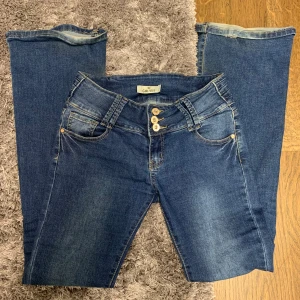 Blå jeans från Girl Vivi med knappar - Snygga blå jeans från Girl Vivi med tre dekorativa knappar framtill och klassiska fickor. Jeansen har en normal passform och är tillverkade i en bomullsblandning med lite stretch för extra komfort. Den är i en fransk storlek och då e den mindre en vad det står så skicka gärna och fråga om mått.