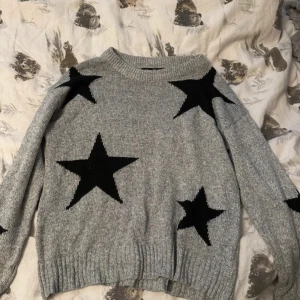 Grå stickad tröja med svarta stjärnor från SHEIN - Säljer en grå stickad tröja från SHEIN med stora svarta stjärnor som detaljer. Tröjan har rund halsringning och långa ärmar. Perfekt för dig som gillar en trendig och mysig look!